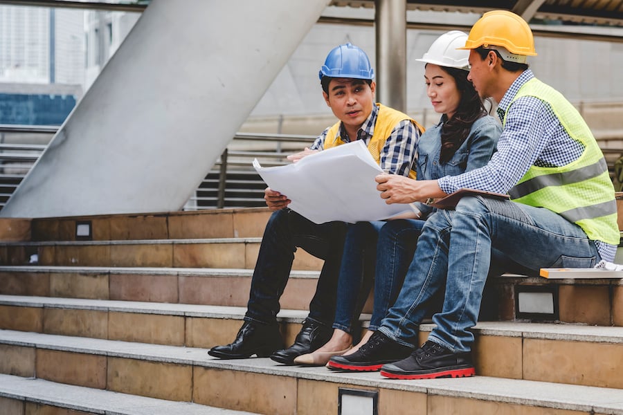 Three manufacturing workers sitting on stairs outside going over a drawing