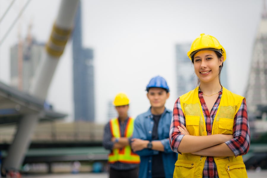 Three construction workers in safety vests and hard hats standing outside at a construction site